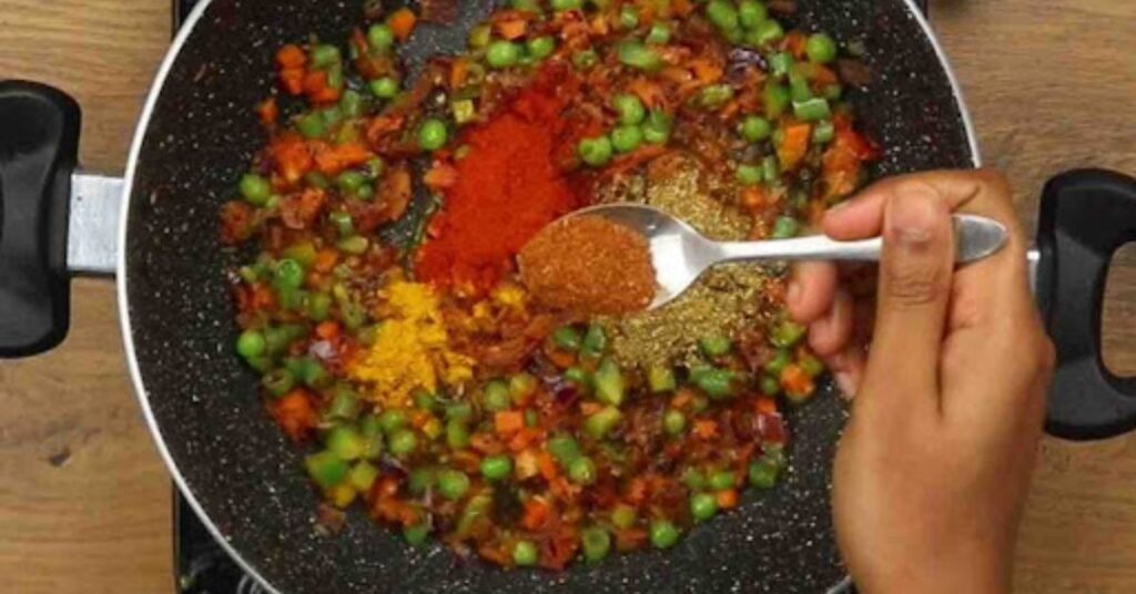 “Adding spices and mixed vegetables for easy vegetable biryani recipe in cooking pot with turmeric chili and garam masala”