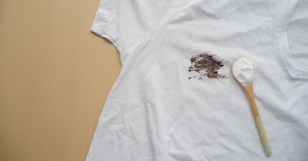 Grease stain on fabric being cleaned with dish soap and baking soda in a kitchen setting.