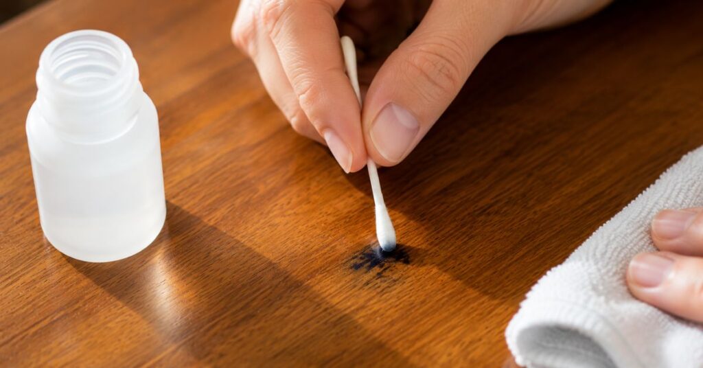 Removing an ink stain from wooden furniture using rubbing alcohol and a cotton swab.